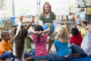 Kindergarten teacher and children with hands raised in library in Kindergärten, Schulräumen, Ausbildungsstätten – überall dort, wo die Gesundheit unserer Kinder und Jugendlichen geschützt werden sollen vor Viren, Keimen und Luftschadstoffen aller Art. Dort wo es um unseren Nachwuchs geht. Die Eltern werden es honorieren.